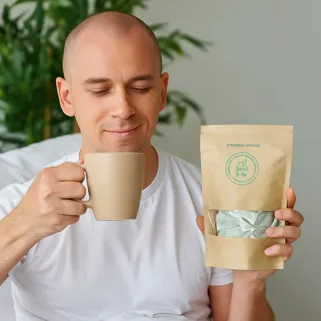Uomo rilassato che gusta una bevanda calda e mostra una confezione di artemisia annuale benessere naturale.